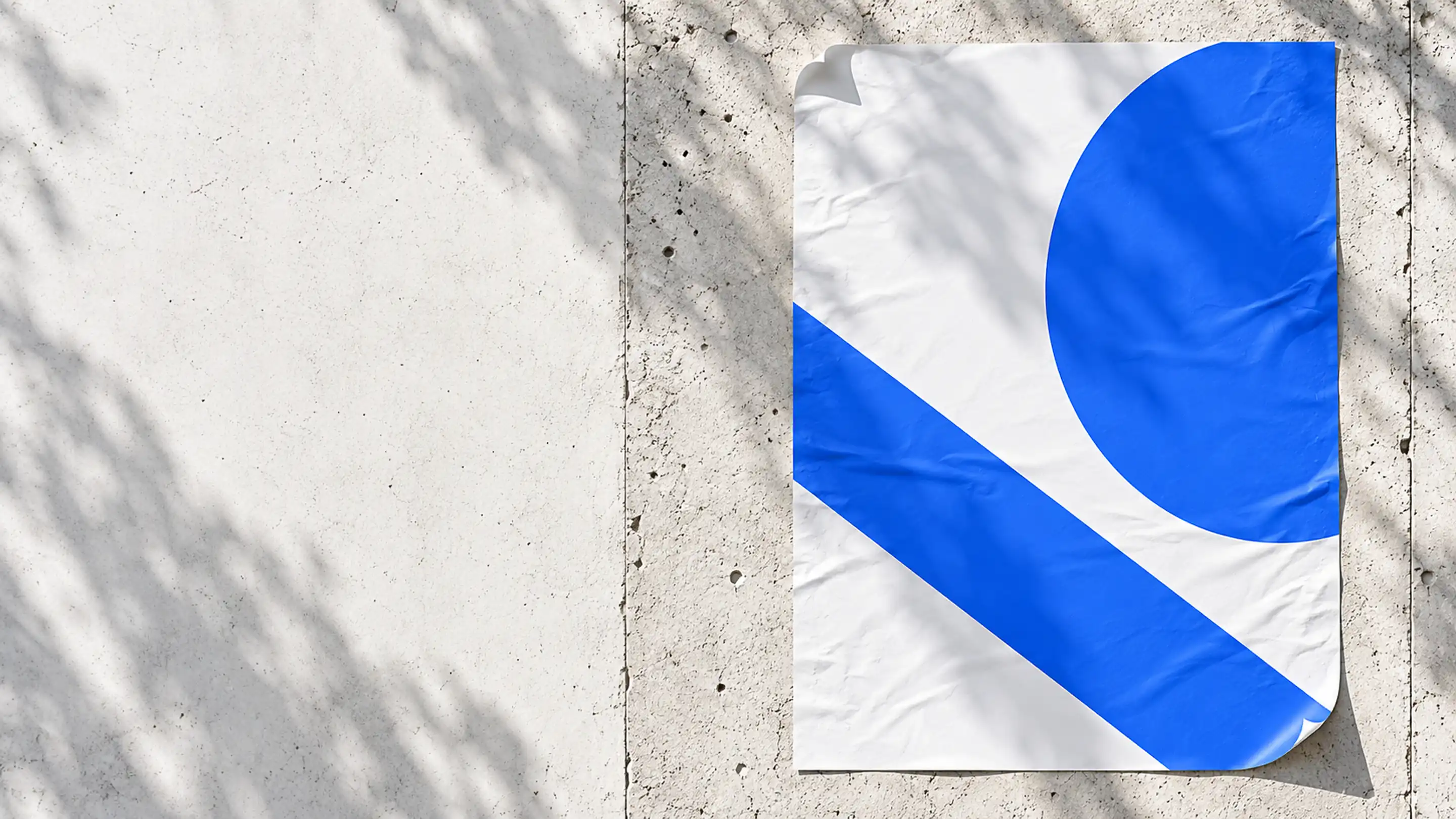 A large poster pasted on a sunlit concrete wall, carrying one electric-blue diagonal band and a blue circle cropped by the poster's edge, with leaf shadows falling across the wall